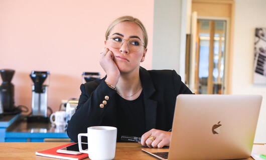 Une femme portant des lunettes réfléchit au contenu de sa lettre de démission à sa table devant son ordinateur et son café.