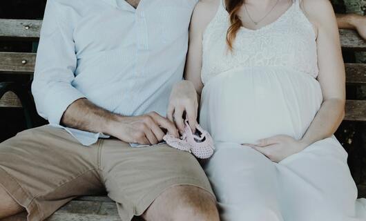 Un homme tient des chaussures d’enfant avec sa femme enceinte après avoir écrit une lettre de demande de congé parental.