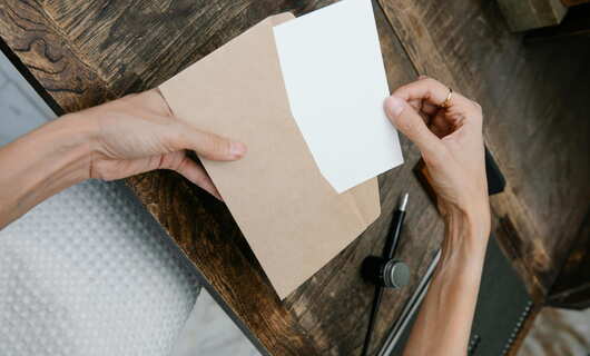 Une dame, entourée par ses outils auprès de sa table, retire une lettre d'une enveloppe marron qu'elle vient de recevoir de son mari depuis l'Algérie.