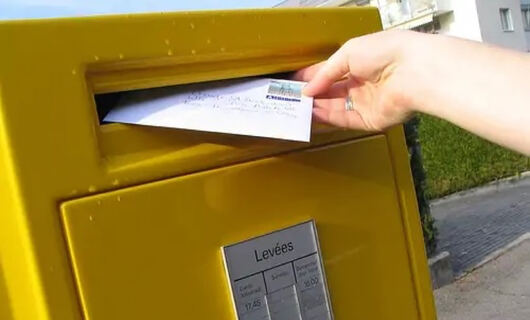 Une femme envoie une lettre recommandée avec avis de réception depuis une boîte aux lettres 