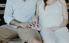 Un homme tient des chaussures d’enfant avec sa femme enceinte après avoir écrit une lettre de demande de congé parental.