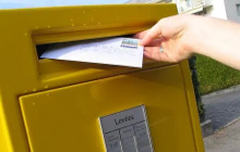 Une femme envoie une lettre recommandée avec avis de réception depuis une boîte aux lettres 